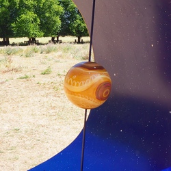 A close-up of the Jupiter model, which is a large sphere painted in shades of orange and brown to match Jupiter itself. The side closest the viewer has a reddish patch representing the Great Red Spot, a major storm on Jupiter.